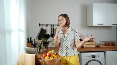 Kafkasyalı anne, modern mutfakta dizüstü bilgisayarda yemek tarifine bakarken salata yapmak için yemek hazırlıyor. Yetenekli ev bekçisi taze sebze kullanarak kahvaltı hazırlıyor. Pedagoji.