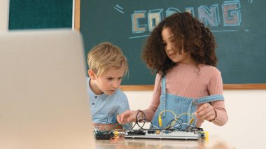 Akıllı kız tornavida kullanarak elektronik tahtayı tamir ederken ayakta duruyor. Mutlu öğrenci ve mutlu beyaz çocuk elektrik sistemini denetlemek için birlikte çalışıyor. Gemide çalışan meraklı çocuklar. Pedagoji.