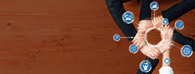 Bu resim, dairesel bir grafiği çevreleyen çeşitli ellerle birleşik bir takım çalışması sergiliyor. Sıcak, ahşap bir zemindeki işbirliği, strateji ve iş büyümesini simgeler. Dostluk