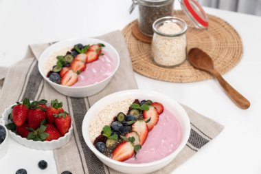 Meyvelerin sunduğu yoğurt malzemelerini çilek, yulaf, kuru üzüm ve nane şekeriyle süslenmiş Chia tohumu ile beyaza boyarız. Pembe arka plan. Sağlıklı süt ürünleri seti. Bireysel.