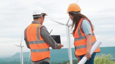 Erkek ve kadın mühendisler kırsal kesimdeki bir tepenin tepesinde ya da dağda rüzgar çiftliğinde çalışıyorlar. Yenilenebilir ve sürdürülebilir enerjinin gelecekteki üretimi için yenilikçi idealler.