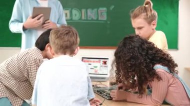 Öğretmenler tableti tutarken ve BTMM teknoloji sınıfında çevrimiçi yazılımı açıklarken ana ekranda dizüstü bilgisayar mühendisliği komut yazısıyla birlikte çalışan çeşitli öğrenci grubu. Pedagoji.