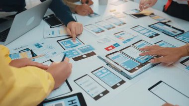 Çeşitli bir ekip etkileşimli bir oturuma katılır, parlak bir çalışma alanında dijital araçlarla dolu bir masada kullanıcı arayüzü prototipleri ve kablolar yaratır. SACTR