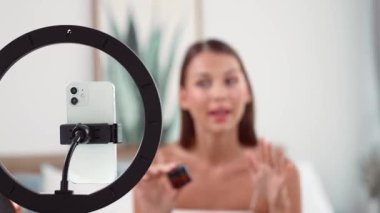 Sosyal medya için güzellik ve kozmetik video içeriği hazırlayan genç bir kadın. Güzellik blogcusu kameraya gülümserken seyircilere ve takipçilere güzellik bakımını gösteriyor. Düzenle