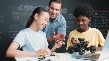 Kafkas öğretmeni dizüstü bilgisayarı işaret ederken araba modelleme sistemini kara tahtada kodlama veya programlama koduyla açıklıyor. Robot inşaatını öğrenen çeşitli öğrencileriniz kutlu olsun. Öğretim