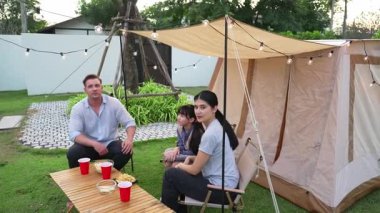 Aile hep birlikte bahçedeki kampta oturup yemek yiyor. Ebeveynler, genç nesil arasında iletişim kurmak ve zaman geçirmek için açık hava kamp faaliyetlerini kullanıyorlar. Uyumsuzluk.