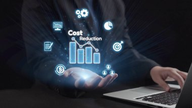 Bir işadamı, mali verimlilik ve stratejik tasarruflara odaklı grafikler ve simgeler yoluyla maliyet azaltma stratejilerini gösteren dijital teknoloji sergiliyor. Dörtgen