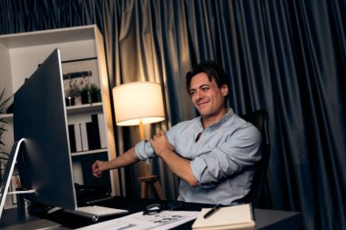 Satış müdürü, geceleri modern ev ofisteki kollarını açıp kapayarak masa başında çalışıyor ve karlı ürünlerin aylık satış raporlarını sunuyor. Bireysel.