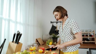 Enerjik anne, mutfak malzemeleri ile çevrili sebzeleri doğrarken modern mutfakta kahvaltı için salata yapıyor. Akıllı kadın temizlikçi yemek pişirir ve yemek hazırlar. Sağlıklı bir yaşam tarzı. Pedagoji.