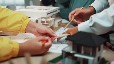 Bir grup profesyonel, bir mimarlık ofisinde, ayrıntılı bina modelini ve planlarını tartışarak yaratıcı takım çalışmalarını ve planlarını sergileyerek işbirliği yapıyor. SACTR