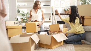 İki kız yeni eve taşınıyor ve oturuyorlar ve kutuları açıyorlar. Ev arkadaşı karton kutuyla çevrili oturma odasında konuşurken dekorasyonu kutudan çıkarıyor. Yeniden yerleştirme. Myrmidon.