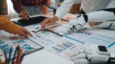 İnsan elini gösteren dinamik bir çalışma alanı sahnesi ve detaylı iş raporları ve grafikleri üzerinde çalışan robotik bir kol yenilik ve takım çalışmasını vurguluyor. Noogenesis