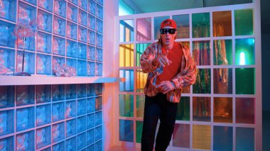 Komik break dansçı kameraya bakarken hiphop 'a doğru serbest adım atıyor. Çılgın mutlu hipster dans edip sokak dansı yaparken Led ışığında günlük kıyafet ve güneş gözlüğü takıyor. Mutluluk.