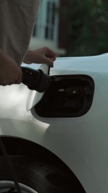 İlerici kadın evdeki elektrikli aracına şarj istasyonu fişi takıyor. EV otomobilleri çevreye yararlı temiz ve yeşil enerji kavramı sağlar.