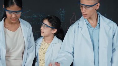 Zeki çocuk deney yaparken deney kabında sıvı karıştırıyor. Akademik öğrenci laboratuvar önlüğü giyerken masada mikroskop ve deneysel ekipmanlarla renkli örnekler koyuyor. Öğretim