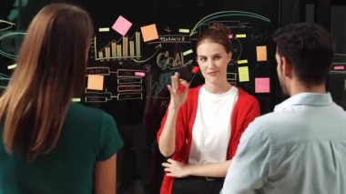 Profesyonel iş kadını yapışkan notlar ve grafikler kullanarak kendine güvenen bir iş kadını sunar. Cam duvarda istatistiksel grafikle duran yetenekli genç ve güzel proje yöneticisi. İzleme