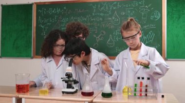 Kafkasyalı öğrenci kimyasal çözüm hazırlarken, yetenekli çocuklar mikroskop altında bakıyorlar. Profesyonel öğretmen, tahtada otururken deney yapıyor. Pedagoji.