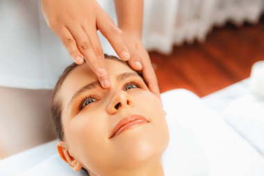 Yakın plan kadın stres önleyici kafa masajı yapmaktan ve lüks tatil beldesi veya otel spa salonundaki modern ışık ortamında yüz güzelliği eğlencelerini şımartmaktan zevk alıyor. Sessiz.