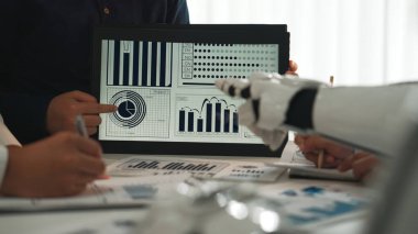 Modern ofis ortamında teknoloji ve yenilikleri vurgulayan, insan ve robot işbirliğiyle veri görselleştirmesini gösteren dinamik bir iş toplantısı. Noogenesis