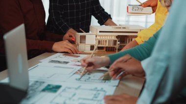 Bir tasarım projesinde işbirliği yapan çeşitli mimarlar grubunu gösteren canlı bir sahne, planlama oturumunda planlar ve fiziksel bir model kullanılıyor. SACTR