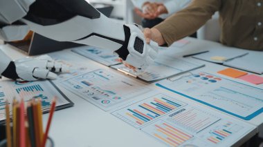 Teknolojinin ve insan işbirliğinin geleceğini sembolize eden, veri tabloları ve belgelerle çevrili modern bir ofiste bir robot bir insanla tokalaşıyor.