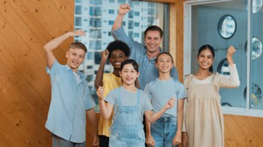 Akıllı öğretmen ve çeşitli öğrenciler kameraya el sallarken ayakta duruyorlar. Karışık ırkları olan liseli çocukların olduğu yetenekli bir eğitmen. Kıyafetleriyle selamlıyor ve neşeli bir şekilde gülümsüyor. Öğretim.