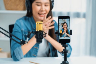 Asyalı sunucu canlı yayında canlı yayında canlı yayında sosyal medyada kulaklık takarak konuşuyor. Dinleyicileri modern stüdyoda koçluk yaparak selamlıyor. Taktik.