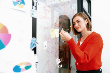 Profesyonel çekici kadın lider, modern iş toplantılarında beyin fırtınası yaparak zihin haritalama istatistikleri kullanarak yaratıcı pazarlama planını sunarken yapışkan bir nota yapıştırıyor. Tertemiz..