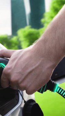 Adam elektrikli araca EV şarj aleti yerleştiriyor ve Green City Park 'taki şarj istasyonunun fütürist akıllı batarya durum hologramından şarj oluyor. ESG şehrinde sürdürülebilir elektrikli araba kullanımı. İnceleyin