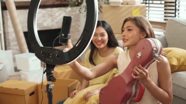 İnternette yayınlanırken gitar kılıfını gösteren ve satan mutlu bir çift. Çekici kız oturma odasında reklam ürünleri için online pazarlama kullanarak yayın yapıyor. Myrmidon.