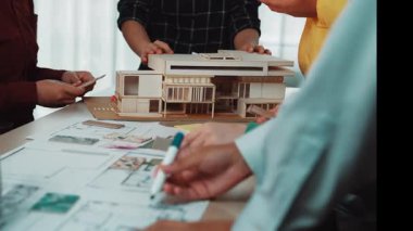 Bir grup profesyonel, modern ofis ortamında mimari tasarım planları ve bina modelini tartışarak takım çalışması ve işbirliği sergilediler. SACTR