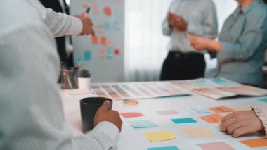 Bir grup profesyonel, modern ofis ortamında renkli notlar, kahve fincanları ve belgelerle dolu bir masanın etrafında ortak bir toplantı yapıyorlar. SACTR