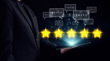 Bir iş adamı, üzerinde beş yıldız bulunan ve müşteri geribildirimi ve dijital çağdaki memnuniyetini gösteren bir tablet tutuyor. Dörtgen