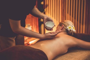 Masör elleri kadının sırtına aroma yağı döküyor. Masözler lüks otellerdeki kaplıca salonundaki müşteriler için yağ masajı prosedürü hazırlıyorlar. Aroma yağı vücut masajı konsepti. Sessiz.