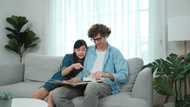 Mutlu kız babaya yaslanır hikaye anlatırken. Genç Asyalı liseli kız birlikte masal kitabı okurken ve kanepede otururken babasını arıyor. Aile eğlence konsepti. Pedagoji.