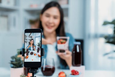 Seçici odaklı akıllı telefon ve gülümseyen genç, güzel Asyalı karışık çilek ve kiraz suyu detoksu değerlendirmesi sosyal medyada sağlıklı ürün tanıtımı sunuyor. Taktik.