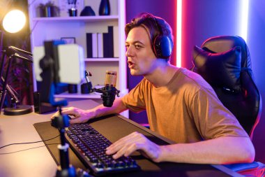 Oyun kanalı, online oyun oynayan akıllı flamalı oyun sunucusu, kulaklık takan, neon ışıklandırma odasındaki takım oyuncusuyla akıllı telefondan canlı yayında konuşan izleyiciler. Bireysel.