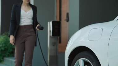 İlerici kadın evdeki elektrikli aracına şarj istasyonu fişi takıyor. EV otomobilleri çevreye yararlı temiz ve yeşil enerji kavramı sağlar.