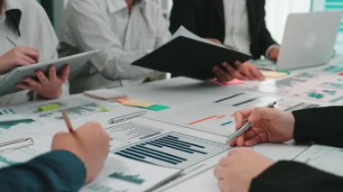 Modern bir ofiste çeşitli profesyonellerden oluşan bir grup, raporları analiz ediyor ve bir iş toplantısı sırasında dijital cihazlar kullanarak stratejileri tartışıyor. SACTR