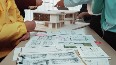 Mimari stüdyo sahnesinde çeşitli ellerin taslakları çizdiğini, yenilikçi tasarımları tartıştığını ve bir inşaat projesi modelini sergilediğini görüyoruz. SACTR