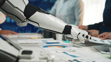 Gelecekçi bir robot kolu modern bir ofiste çeşitli iş raporları ve veri tabloları ile meşgul olarak teknoloji ve kurumsal stratejinin kesişimini vurgular. Noogenesis