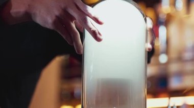 Viski kokteyli sunumunda dumanlı dumanlı dumanlı içki servisi yapan kırpılmış el barmeni içecek tezgahında özel, lezzetli, yaratıcı bir reklam içeceği öneriyor. Vinosity.