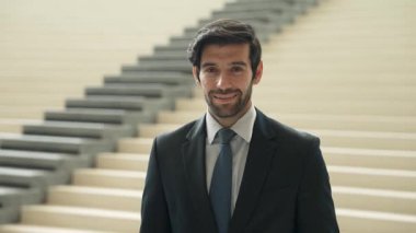 Akıllı iş adamı merdivenlerde kameraya bakıyor. İş elbisesi giyerken kameraya gülümseyen başarılı adamın yakın çekimi. Yönetici, kameraya bak. Hareket eden kamera. Sevinçli..