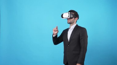 Sanal gerçeklik gözlüğü takan ve mavi arka planda duran iş adamı hologramı tutuyor. Yatırımcı teknolojiyi kullanarak strateji planlarken raporları kontrol ediyor ve denetliyor. Aygıt.