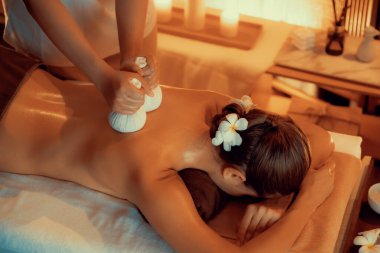 Sıcak bitkisel top spa masaj vücut tedavisi, masör kadın vücuduna nazikçe şifalı bitki torbası bastırıyor. Aromaterapi tesisinin sakinliği ve dinginliği kaplıca salonundaki mumların sıcacık ışığında. Sessiz.