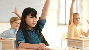 Sınıfta ders çalışan çok kültürlü çocuklarla çevrili öğretmenine sorup cevap veren mutlu kız elini kaldırıyor. Mutlu öğrenci birlikte çalışıyor, oy veriyor, gönüllü oluyor, hocayı arıyor. Pedagoji.