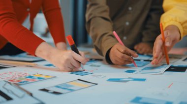 Çeşitli profesyonellerden oluşan bir grup işbirlikçi beyin fırtınası oturumunda, parlak ofis alanlarında işaretleri olan yenilikçi fikirleri kağıda çiziyorlar. SACTR