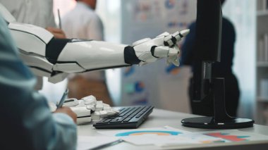 Çağdaş ofisteki bir bilgisayarla etkileşime giren robot kol, iş yenilikleri ve analizlerindeki teknoloji ve takım çalışması arasındaki sinerjiyi vurgular.