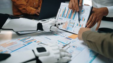 Modern ofis ortamında takım çalışmasının ve yeniliğin vurgulandığı, rengarenk grafiklerle veri analizi üzerinde çalışan insan ve robotları gösteren ortak bir sahne. Noogenesis