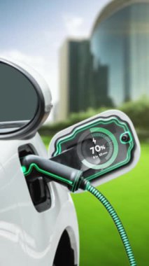EV otomobili, elektrik yükleme istasyonuna bağlanarak yeşil parktaki EV şarj cihazının pil durumu hologramını şehrin gelecekteki ekolojik yaşam biçimi ve temiz enerjinin kullanımı olarak gösteriyor. İnceleyin